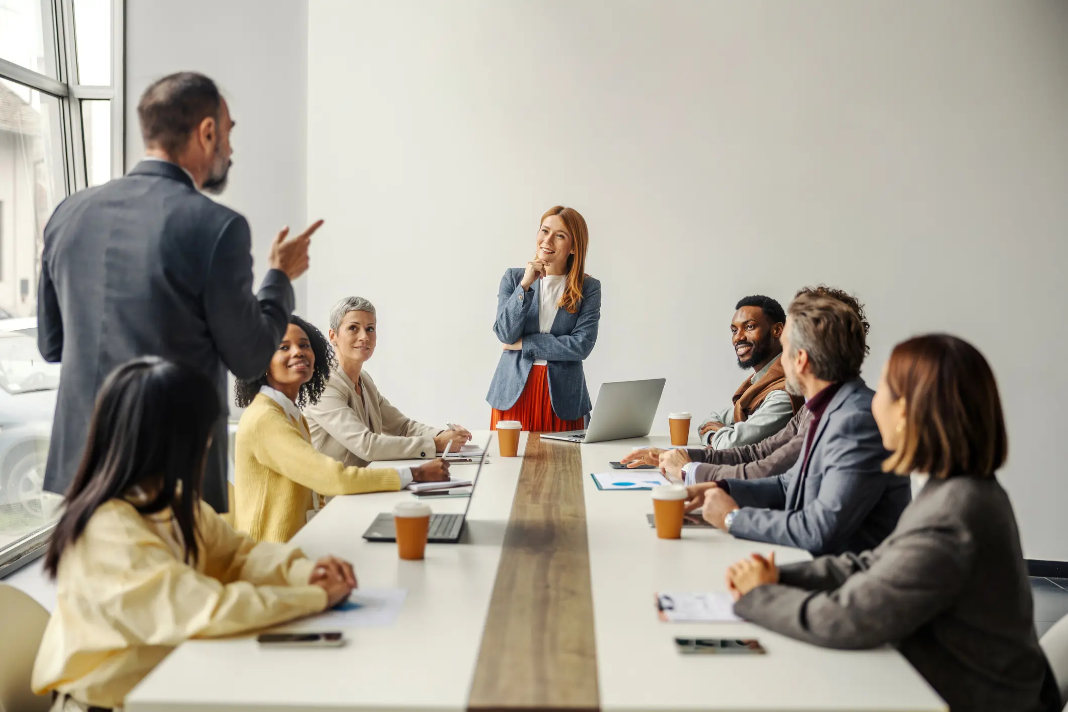 Diverse business team listening to a colleague presenting during a corporate meeting, actively engaging and collaborating on new strategies in a modern office environment